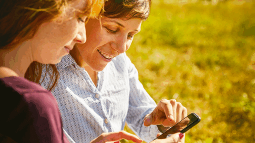 Deux femmes utilisant une application mobile de tourisme en plein air, symbole de la digitalisation des services touristiques.