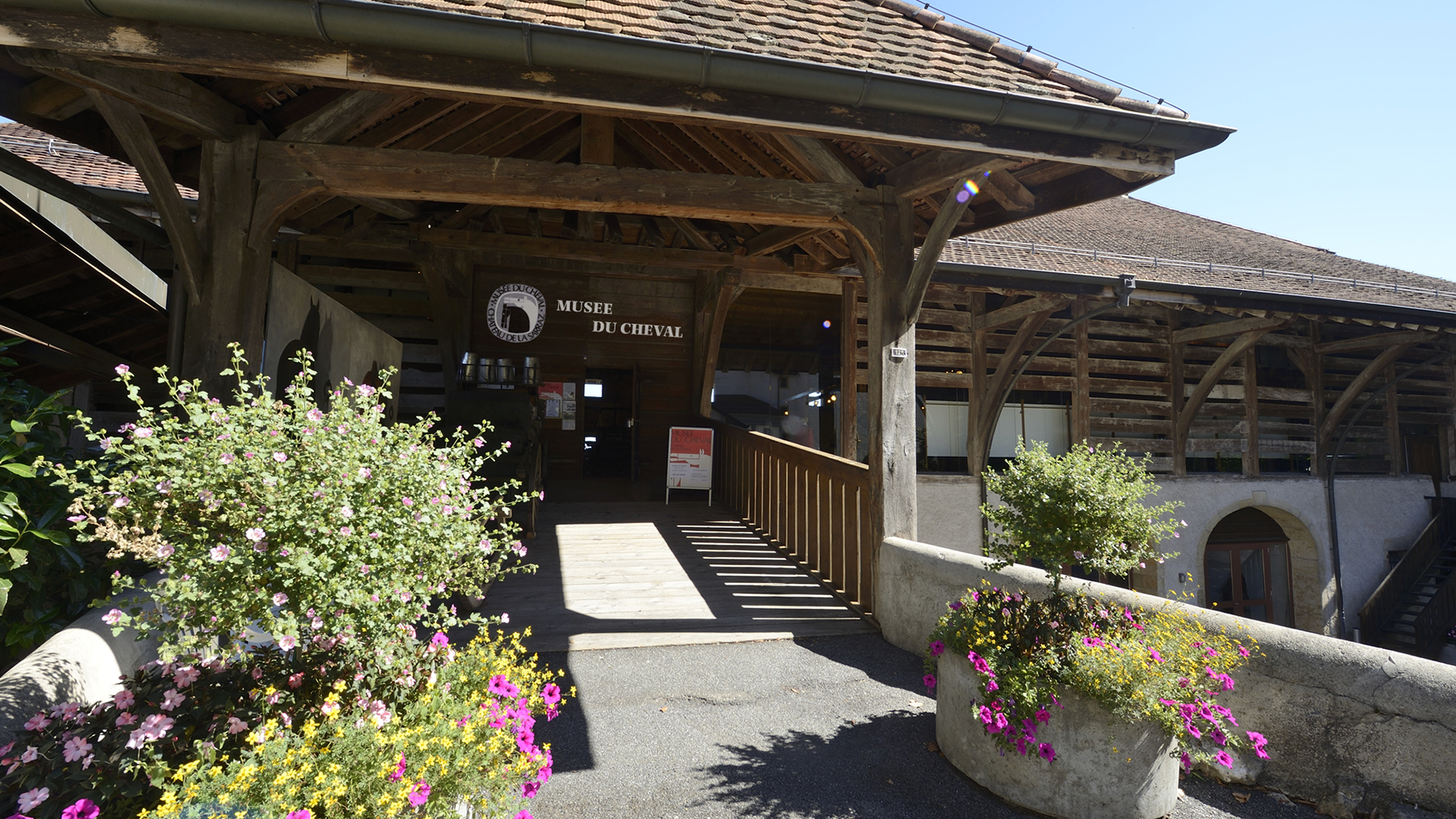 Entrée du Musée du Cheval à La Sarraz, Vaud, Suisse – bâtiment historique en bois avec fleurs colorées.